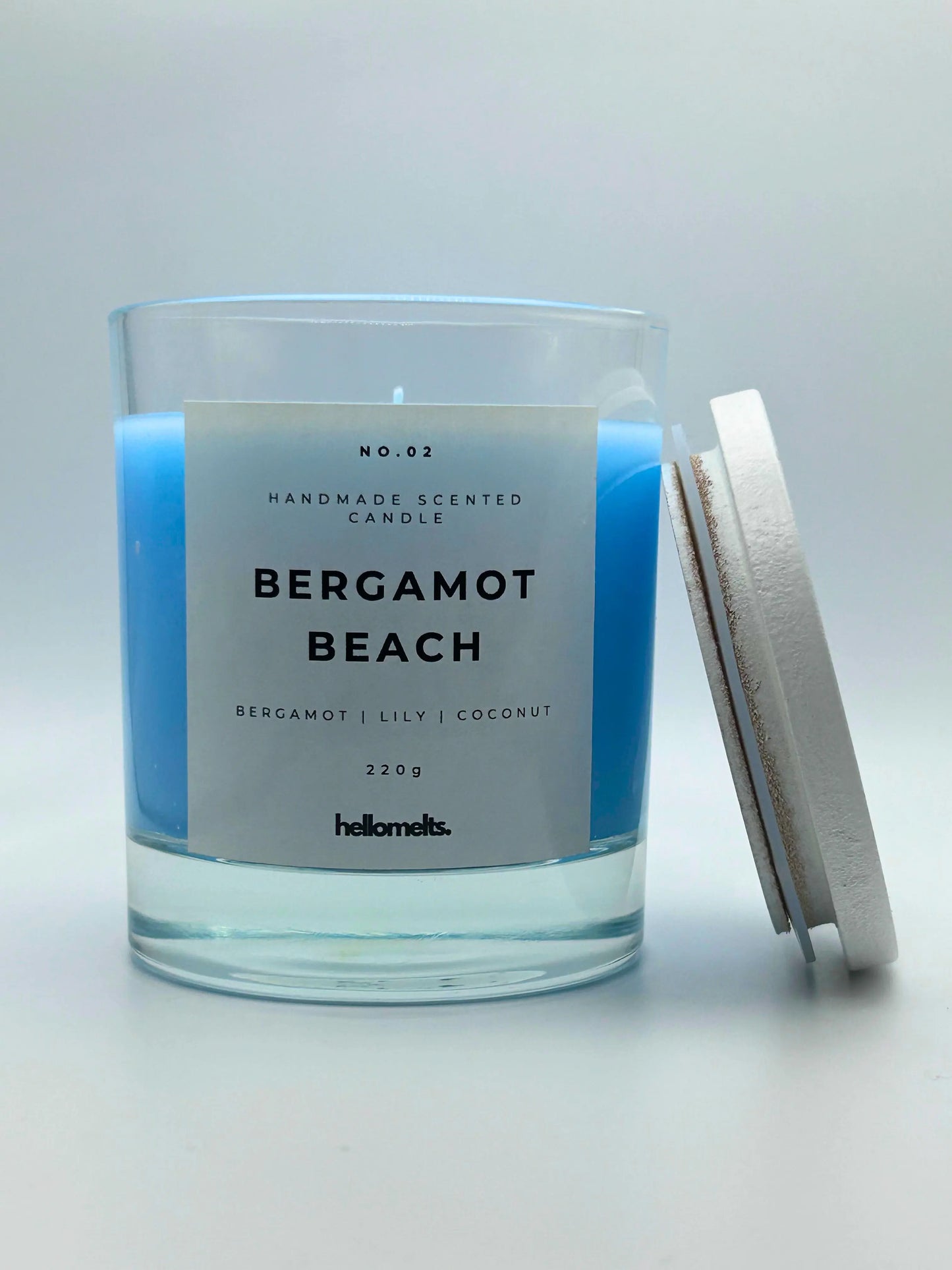 Bergamot Beach 220g candle, with lid beside jar, by Hellomelts, infused with refreshing bergamot, lily and a hint of coconut, in a beach-inspired blue wax.