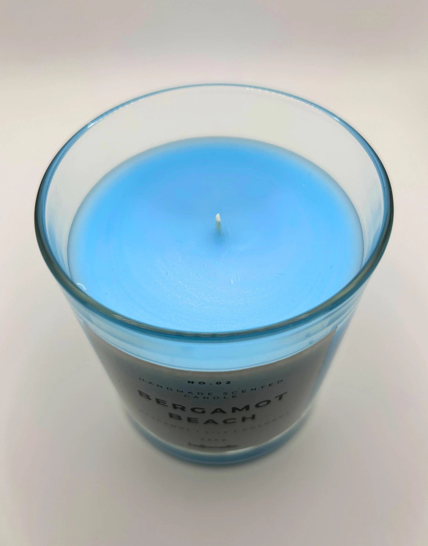 Bergamot Beach 220g candle, showing top of jar with lid off, by Hellomelts, infused with refreshing bergamot, lily and a hint of coconut, in a beach-inspired blue wax.