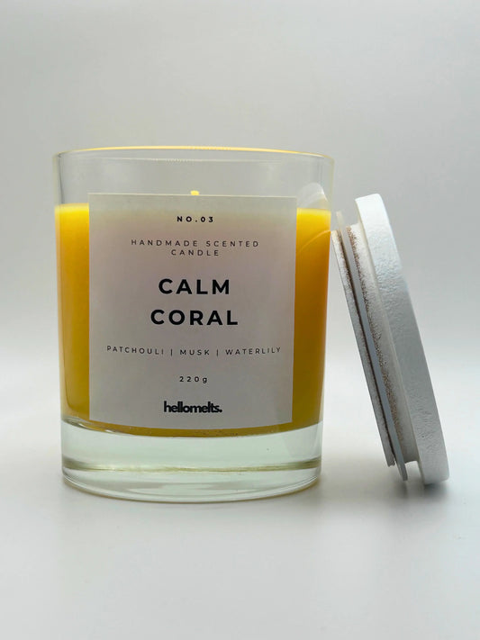 Calm Coral 220g candle, with lid beside jar, by Hellomelts, blending patchouli with soothing scents of musk and a touch of waterlily, in a bright yellow wax.