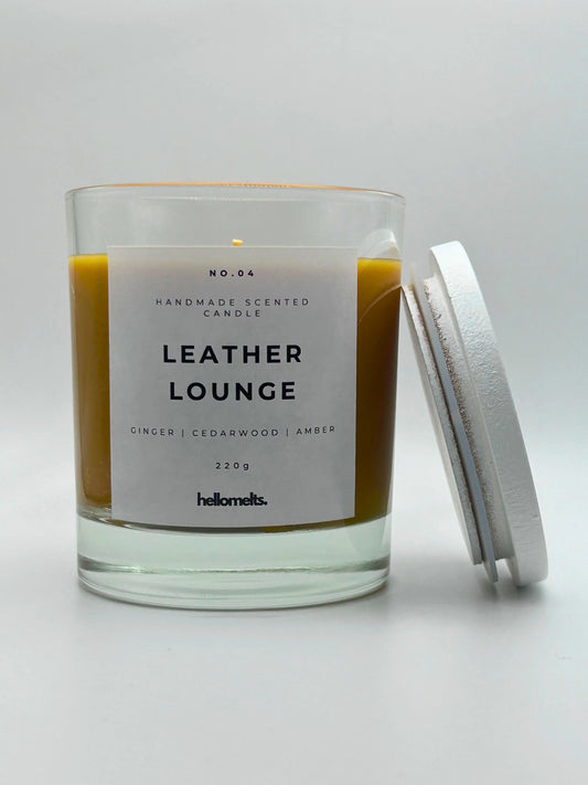 Leather Lounge 220g candle, with lid beside jar, by Hellomelts, infused with notes of ginger, cedarwood, and amber, captured in a brown wax to resemble leather.