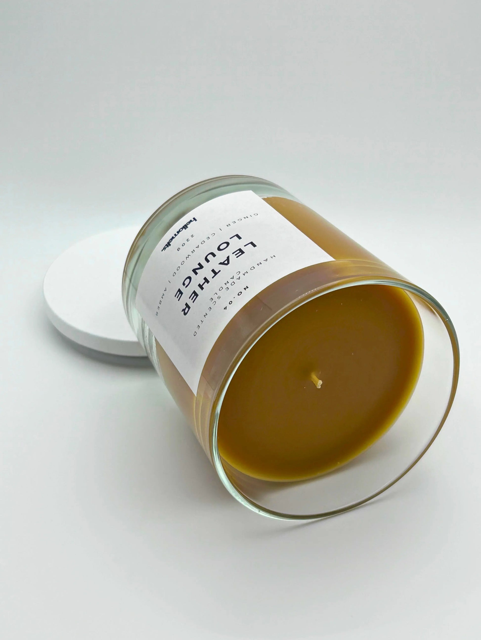 Leather Lounge 220g candle, on its side, by Hellomelts, infused with notes of ginger, cedarwood, and amber, captured in a brown wax to resemble leather.