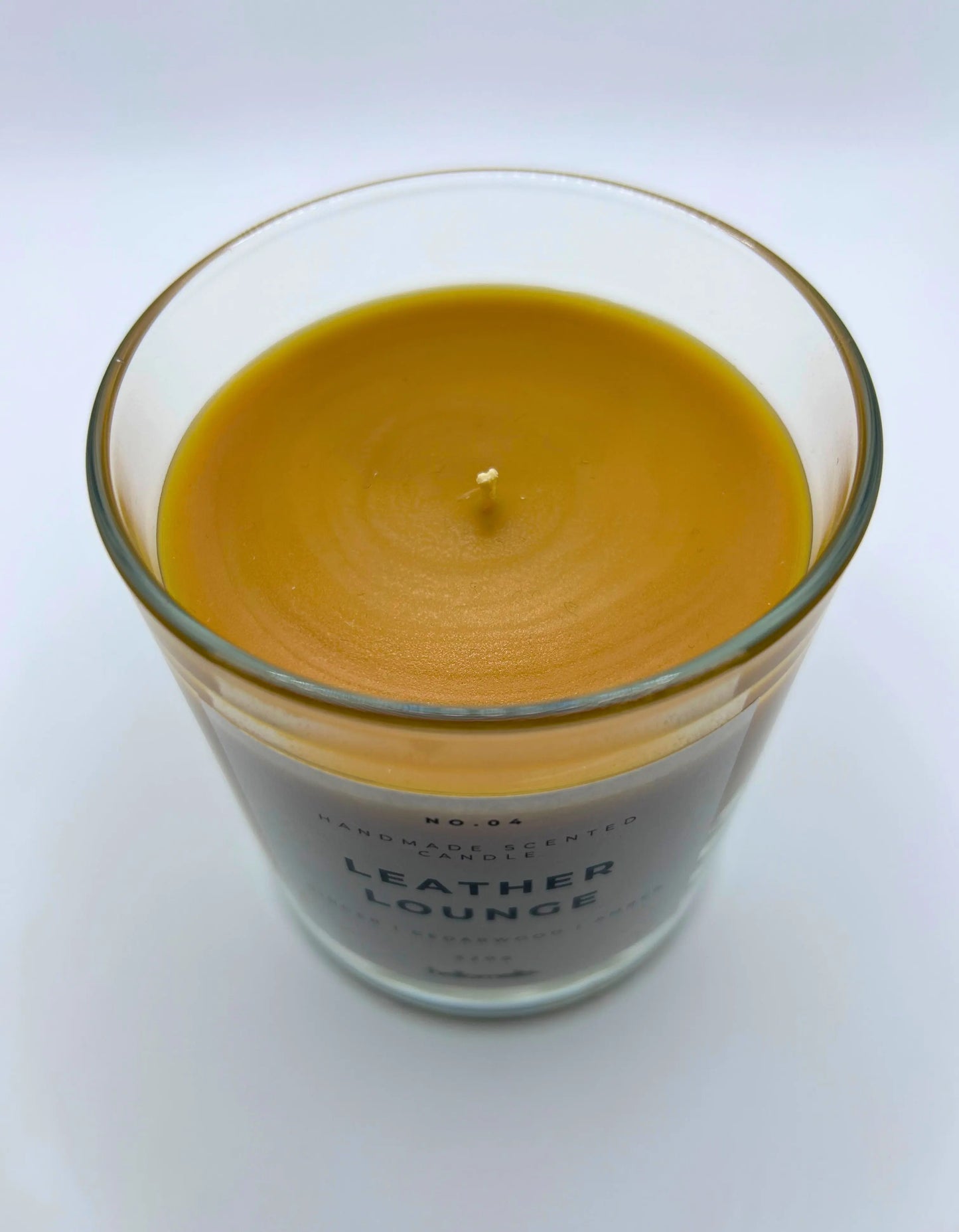 Leather Lounge 220g candle, showing top of jar with lid off, by Hellomelts, infused with notes of ginger, cedarwood, and amber, captured in a brown wax to resemble leather.