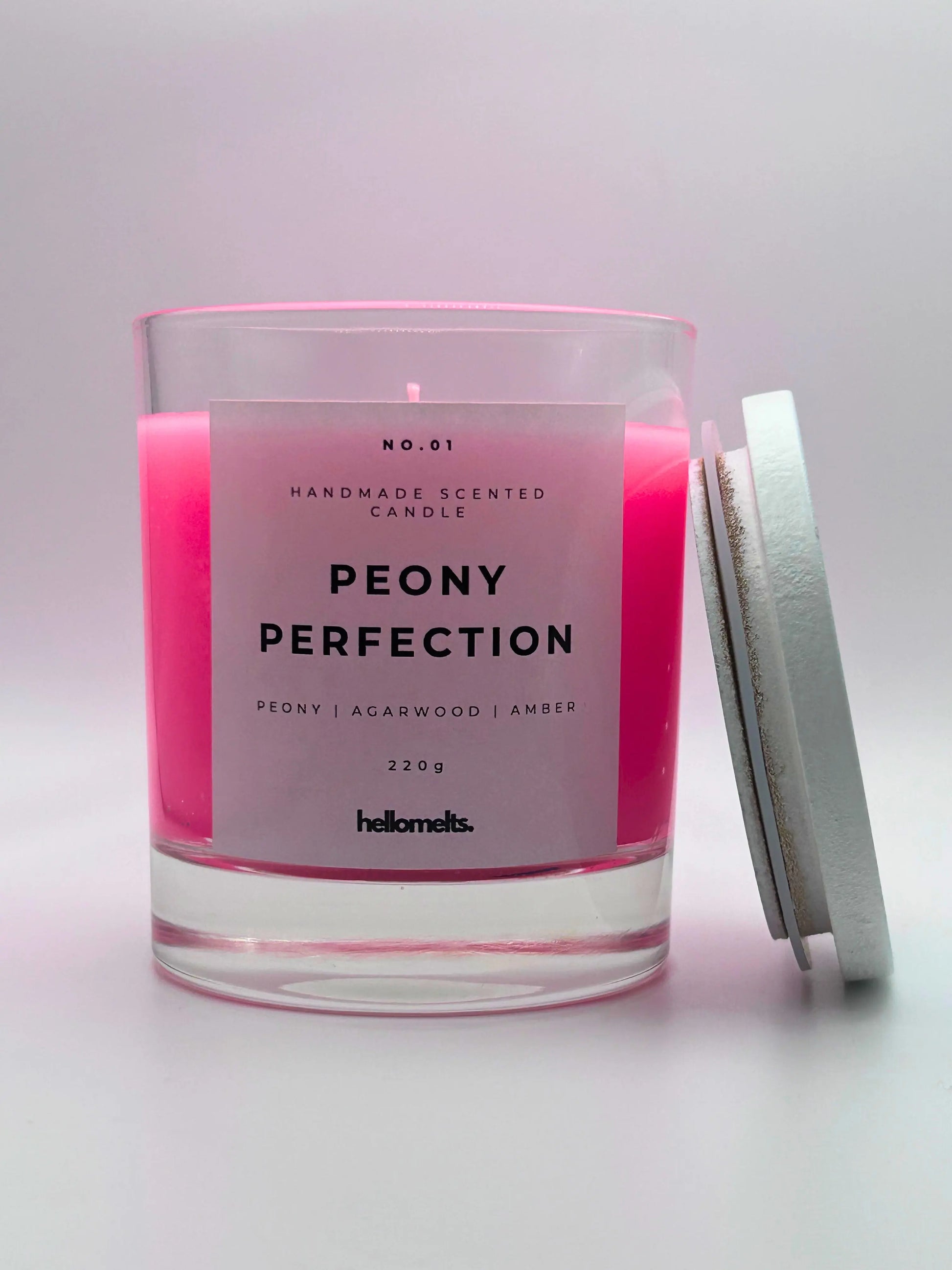 Peony Perfection 220g candle, with lid beside jar, by Hellomelts, exuding delicate peony, luxurious agarwood, and warm amber aromas, in a beautiful bright pink wax.