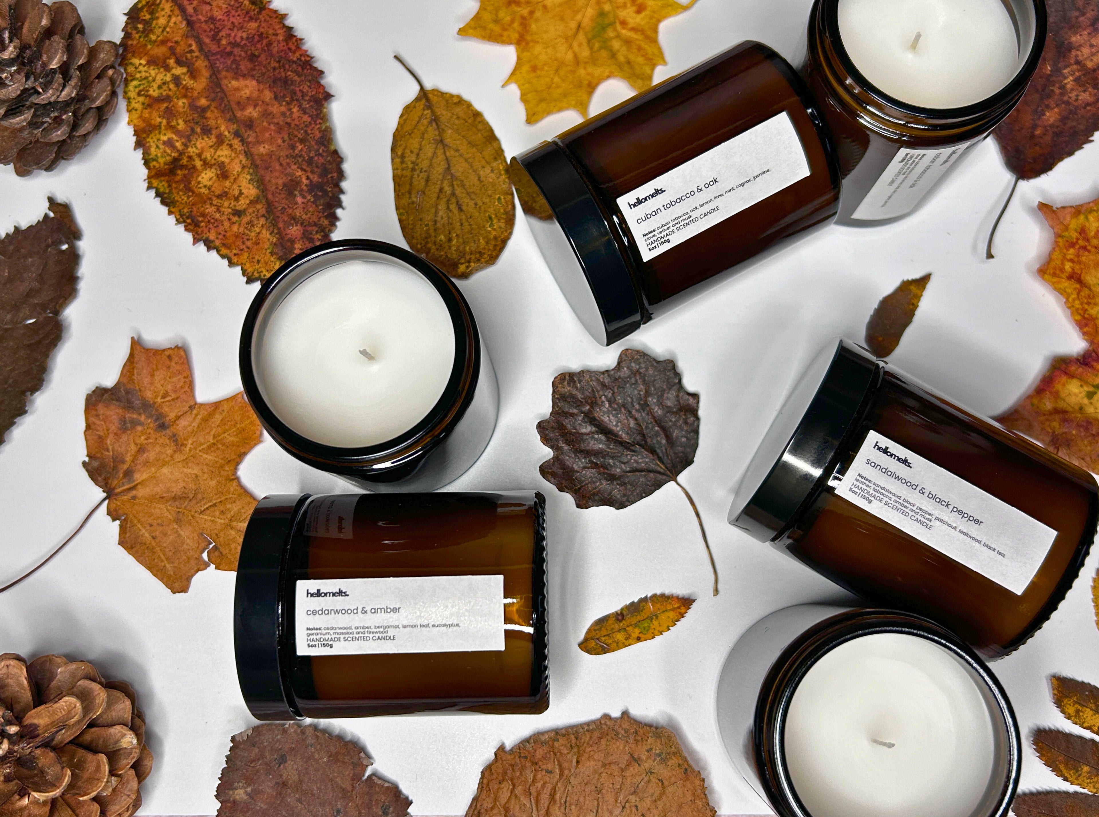 Hand-poured autumn candle collection banner by Hellomelts, featuring Cedarwood & Amber, Cuban Tobacco & Oak, and Sandalwood & Black Pepper candles, surrounded by autumn leaves.