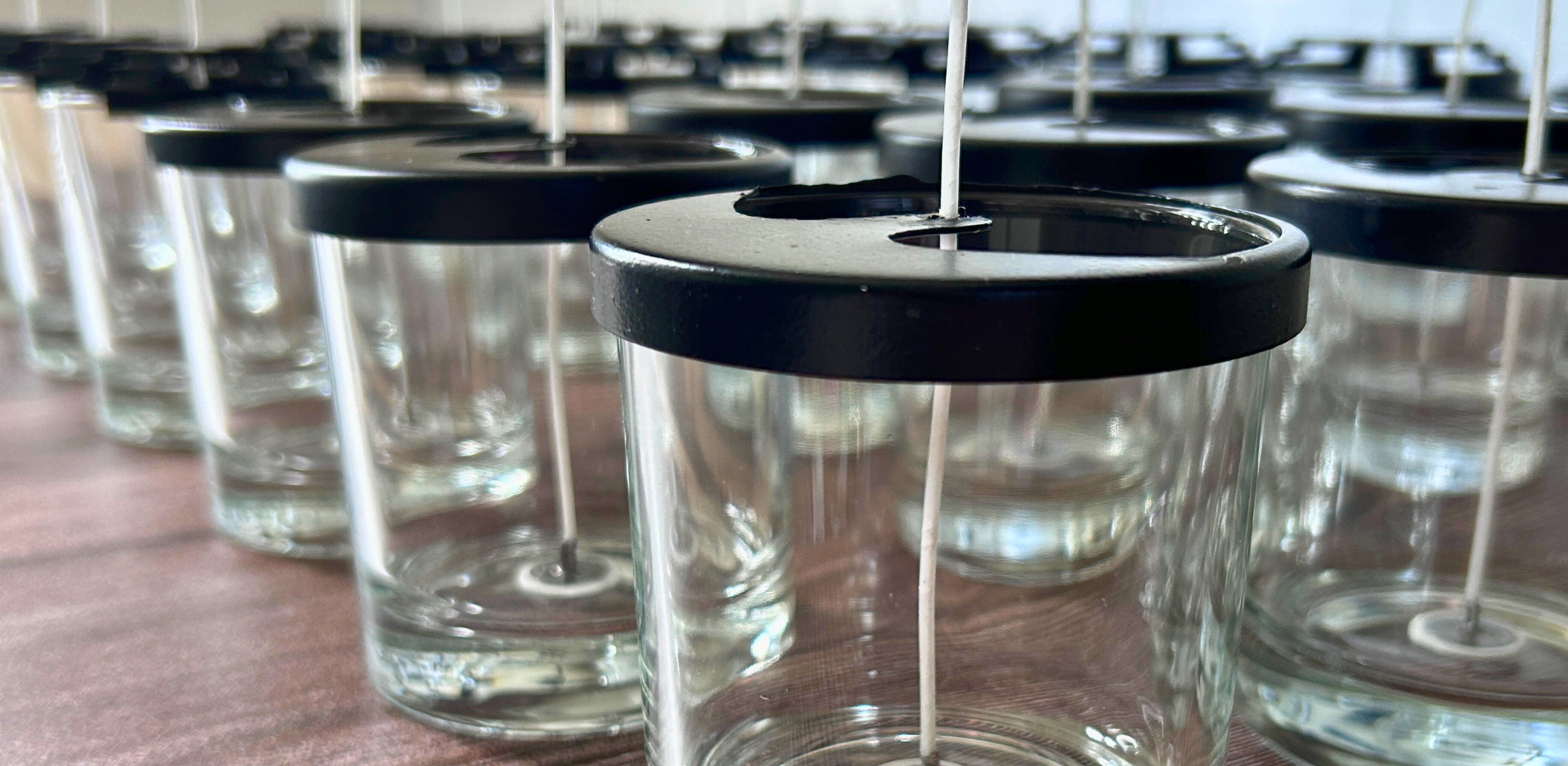 Banner showcasing candle preparation at Hellomelts with rows of glass jars and wicks ready for hand-pouring.